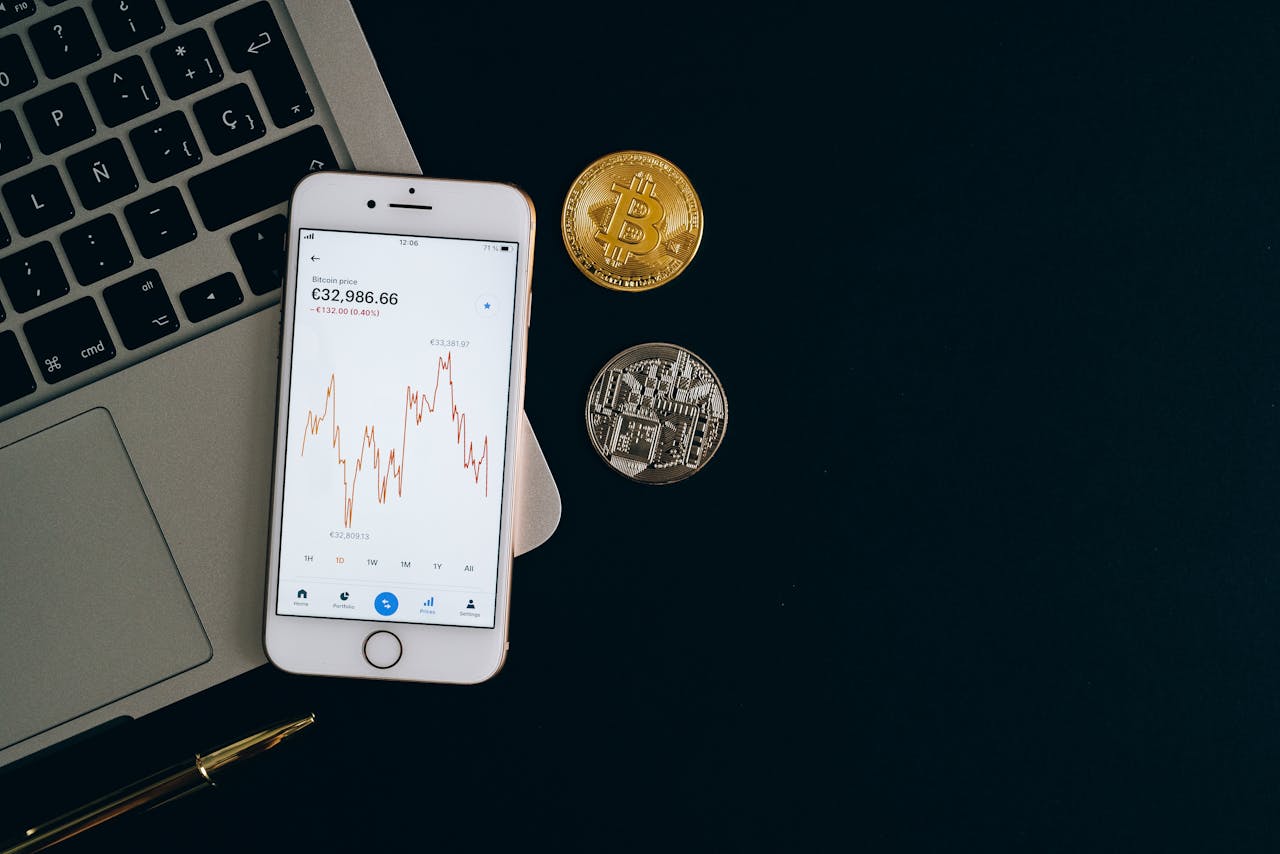 Smartphone displaying Bitcoin price chart alongside Bitcoin and Ethereum coins on black background.